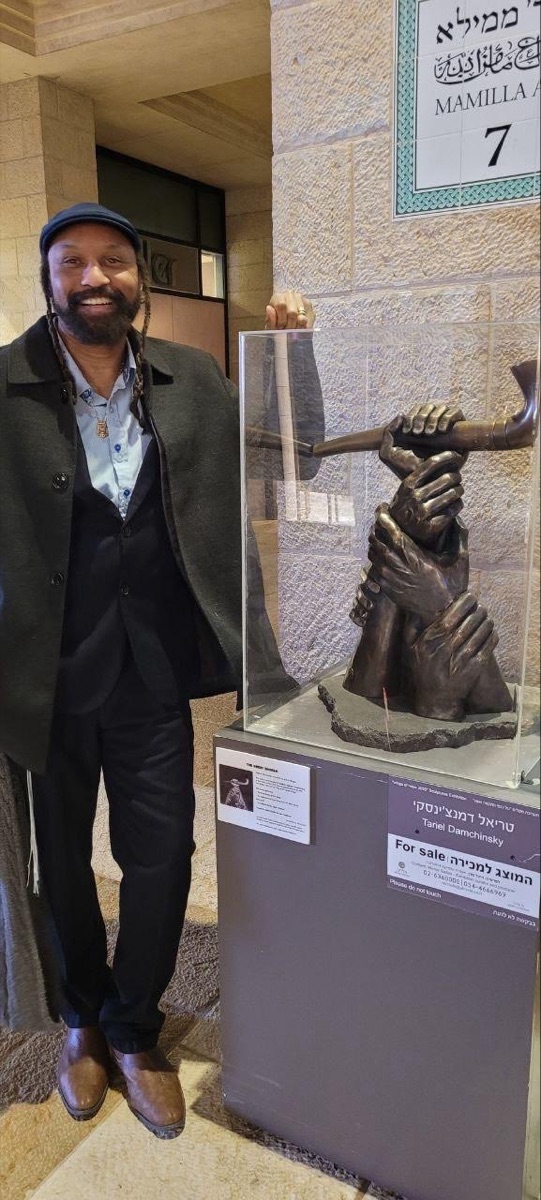 A visitor posing with The Great Shofar bronze sculpture at the Mamilla Mall exhibition, with Tariel Damchinsky nameplate visible